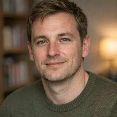 Man in his late thirties, dark-blonde hair, light freckles, calm expression, olive knit…